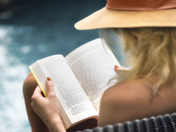 Caucasian woman sitting by a swimming pool and reading a book 