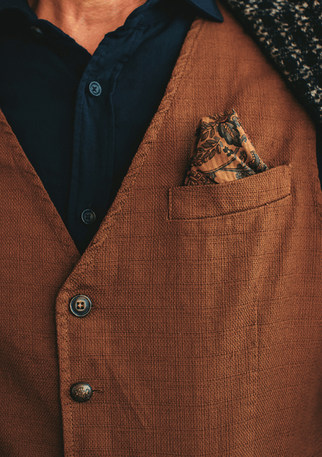 Closeup of crop incognito man wearing woolen checkered brown blazer with dark blue shirt and brown vest with flower pocket square